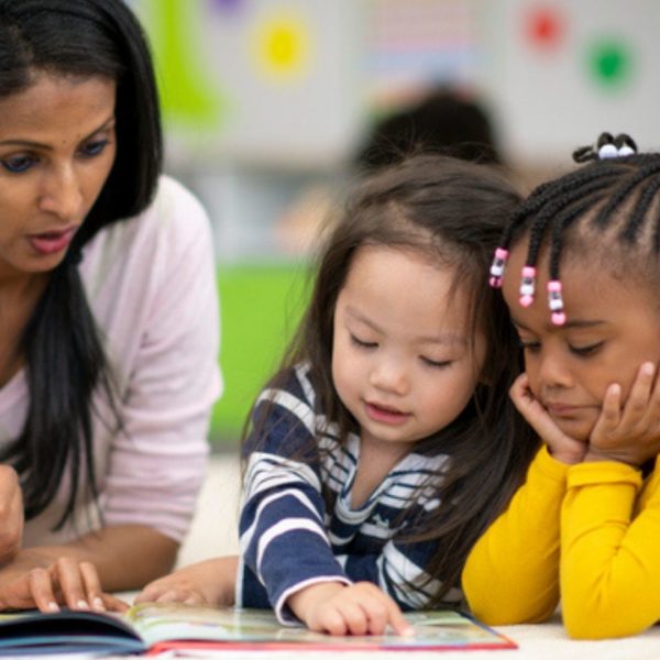A teacher reading a book with two students.