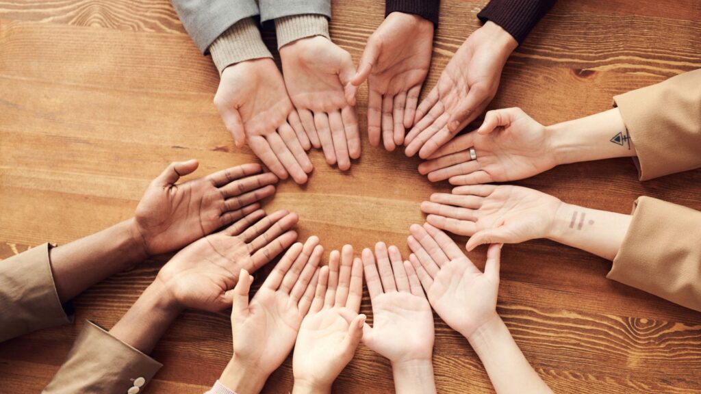 An image of six pairs of hands forming a circle with their palms facing up on the table.