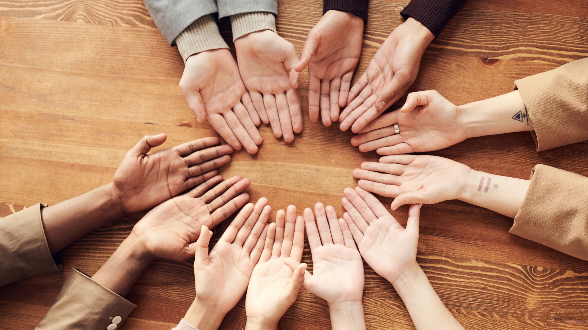 An image of six pairs of hands forming a circle with their palms facing up on the table.