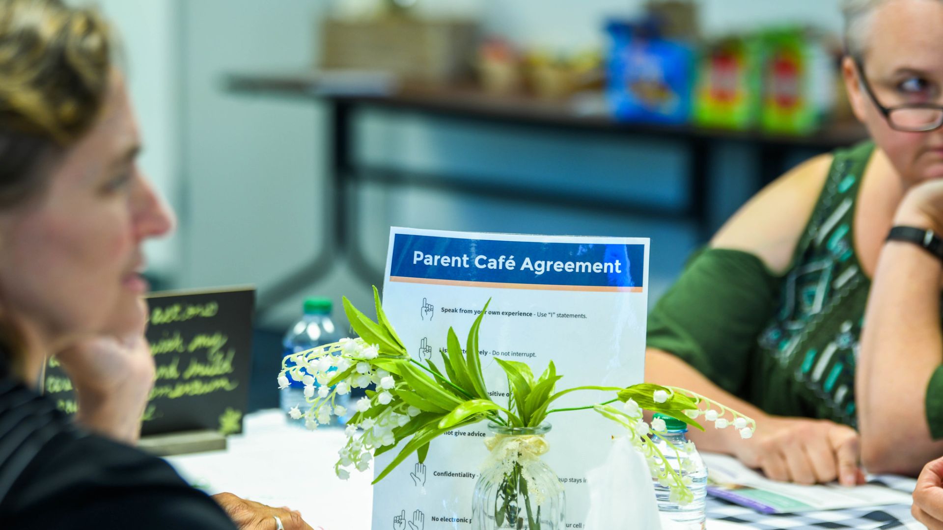 A close up picture of the “Parent Café Agreement” that is a centerpiece at our Café events with two females at the table engaged in conversation.