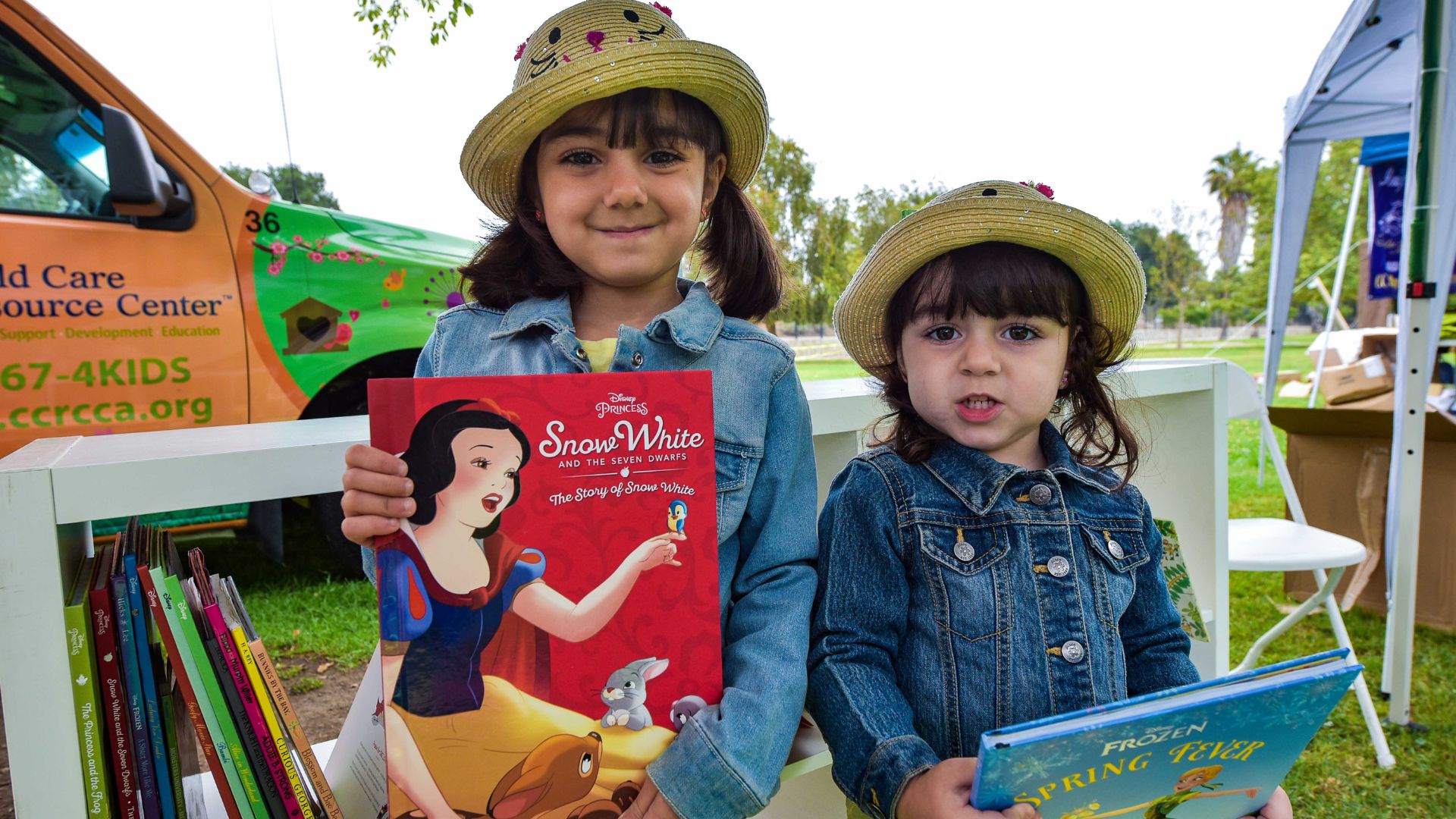 An image from CCRC’s Annabelle Godwin Play Day with two sisters each holding a book (Snow White, and Frozen) that they got to take home for free at our family play day.