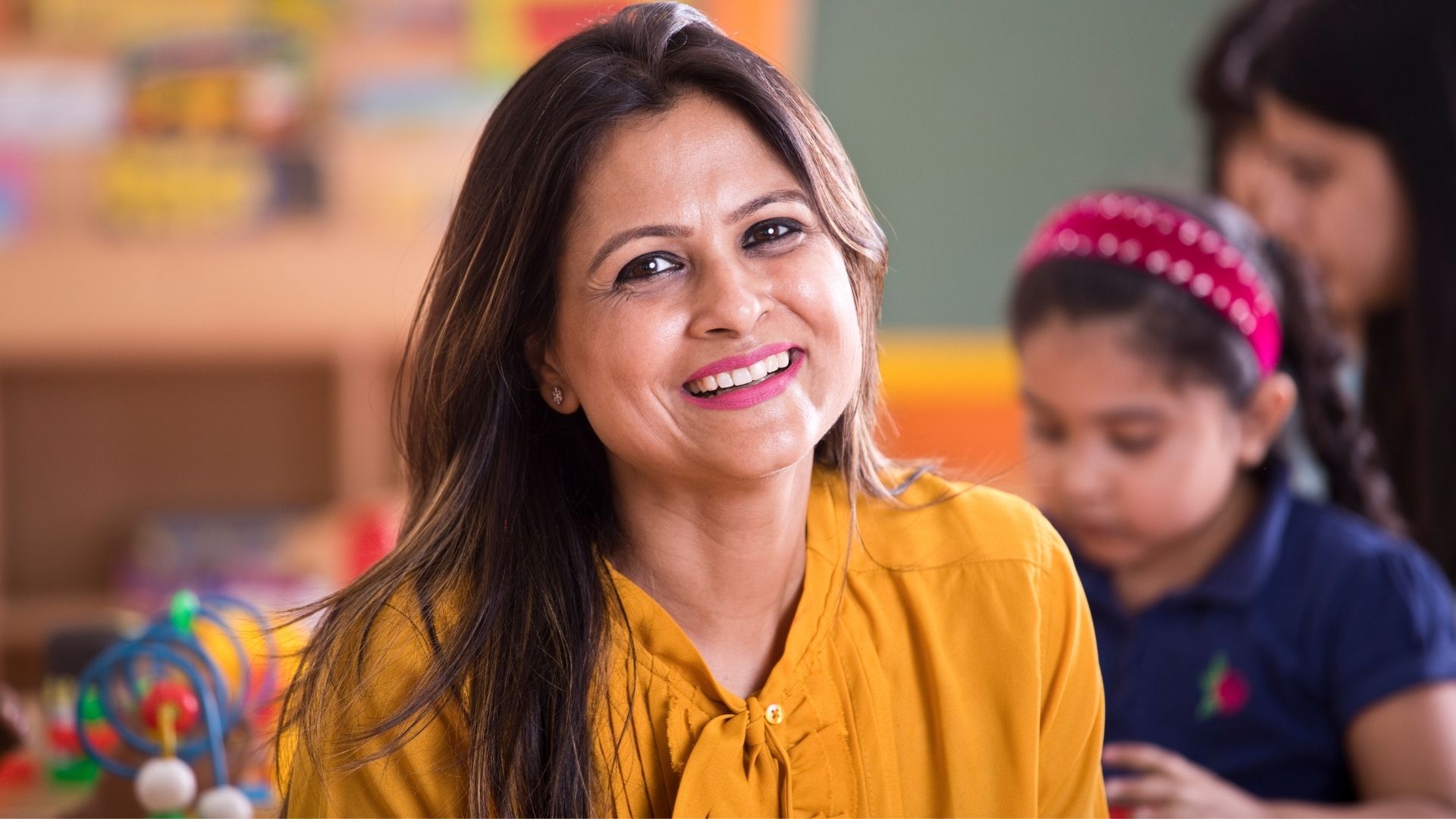 An image of a female teacher smiling at the camera in her classroom.