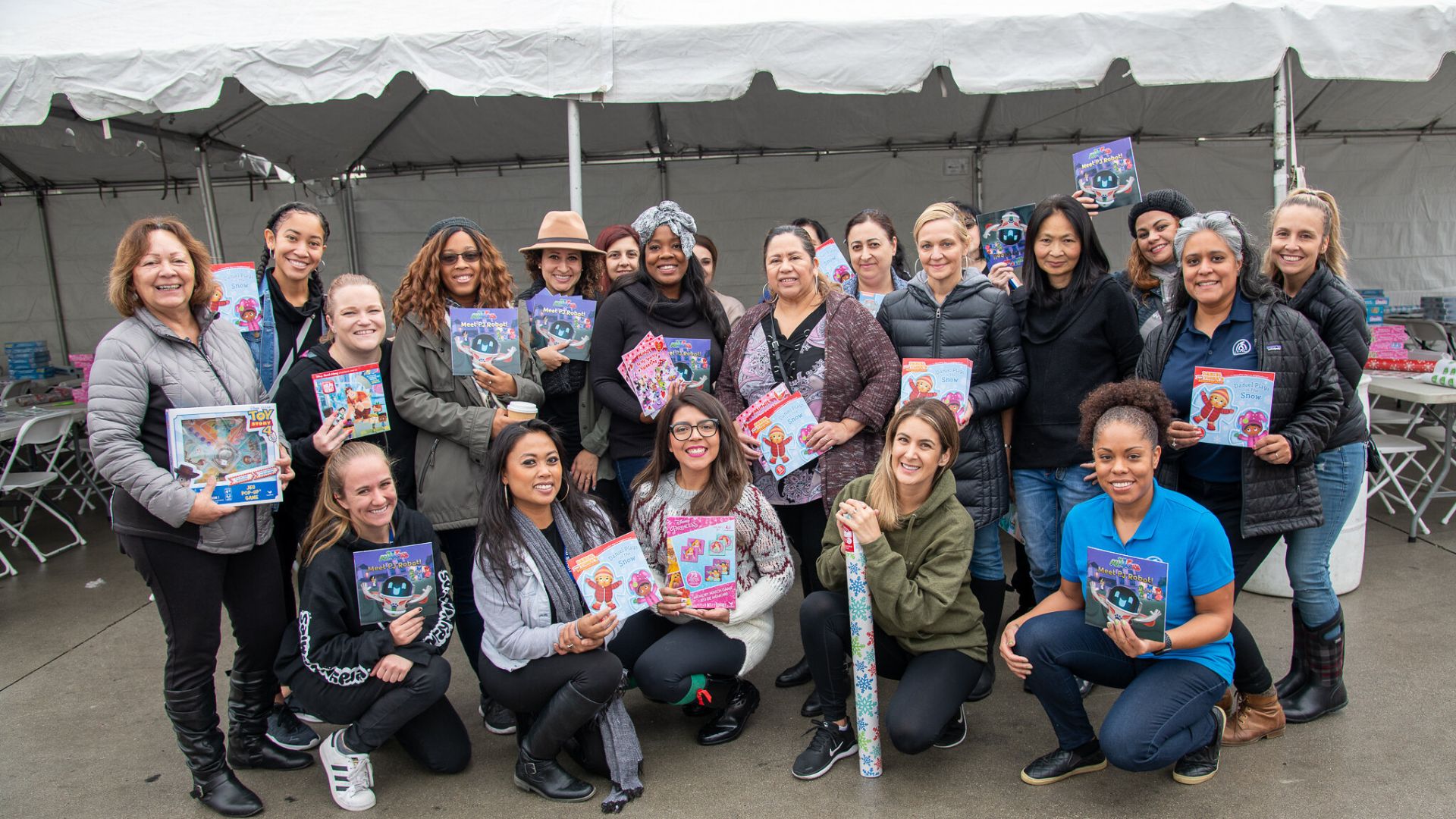 A group picture from a previous CCRC holiday wrapping event with volunteers holding up books or wrapping paper taken in Van Nuys CA.