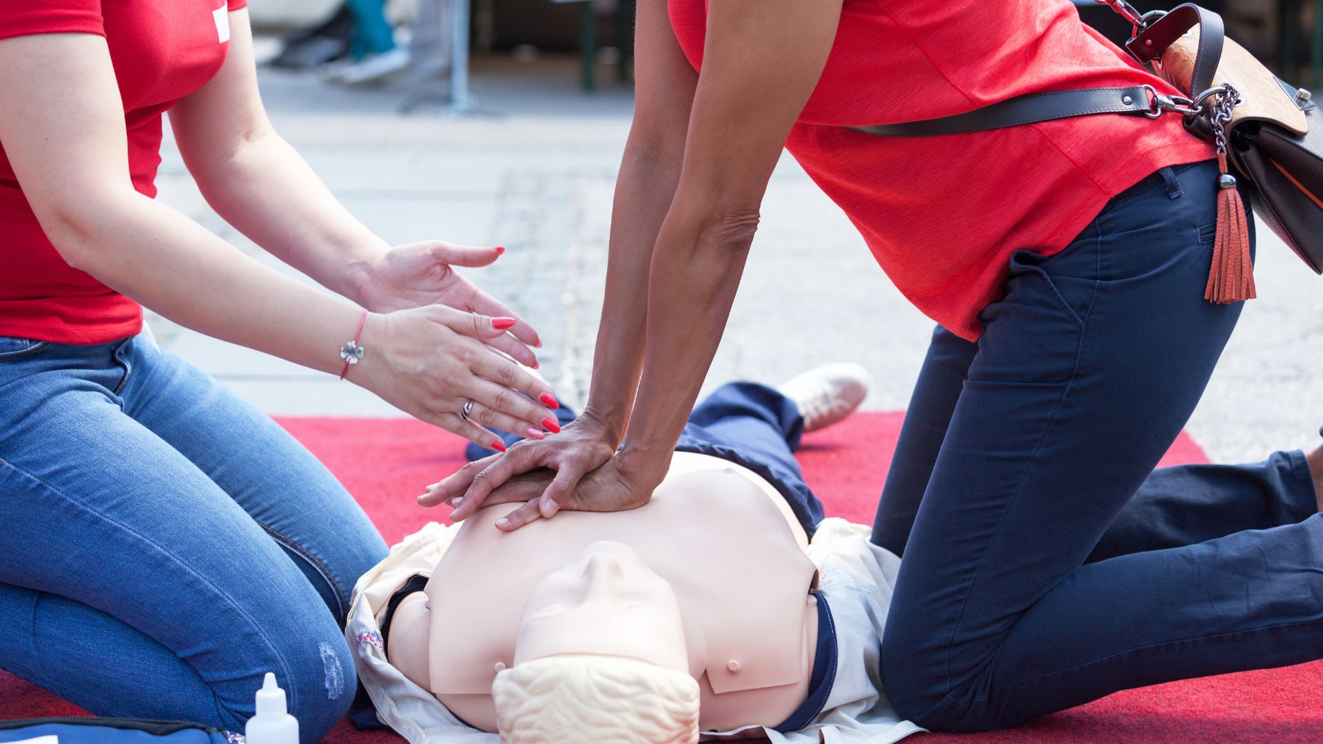 An image of a student learning how to perform CPR with an instructor offering guidance.