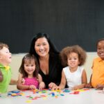 Teacher and six students at the table playing with puzzle pieces with a blackboard behind them.