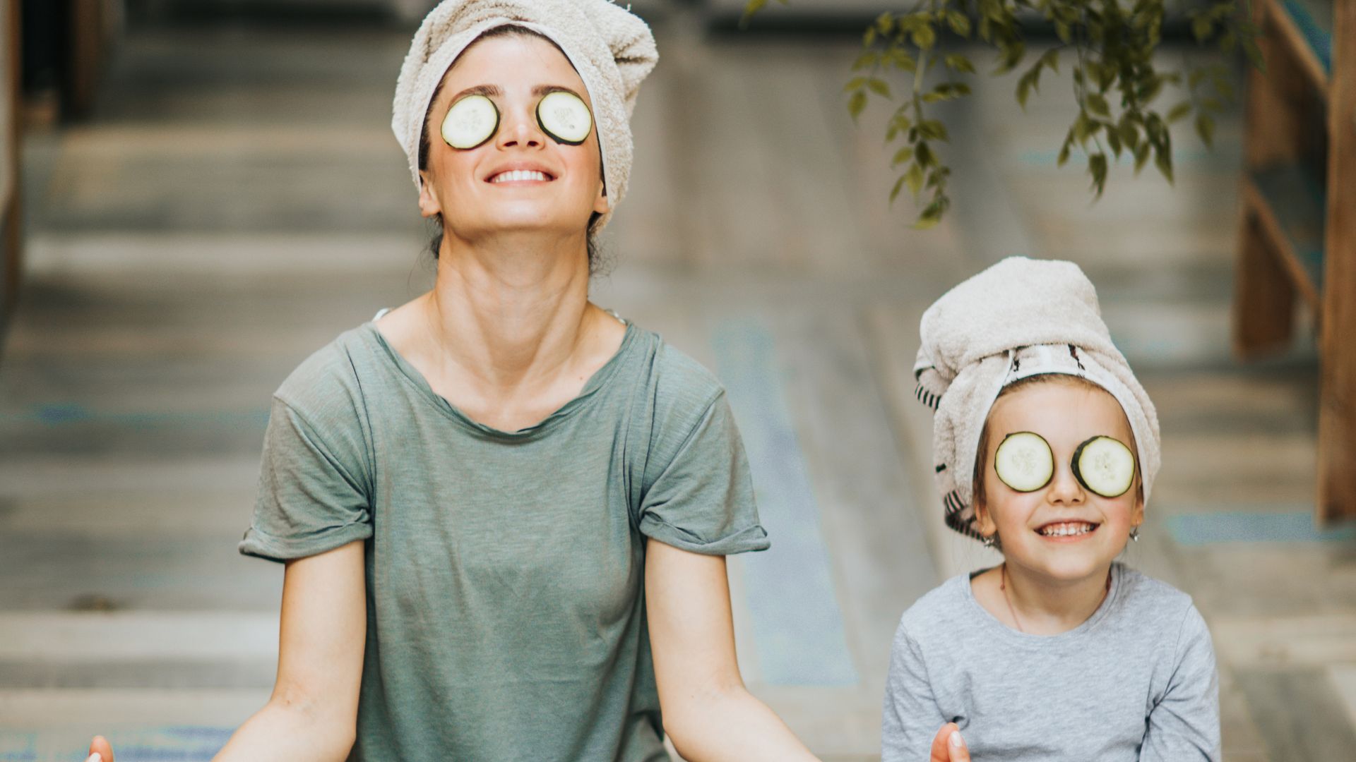 An image of a mother and daughter with cucumbers over their eyes smiling as they take a few moments to meditate as a form of self care.
