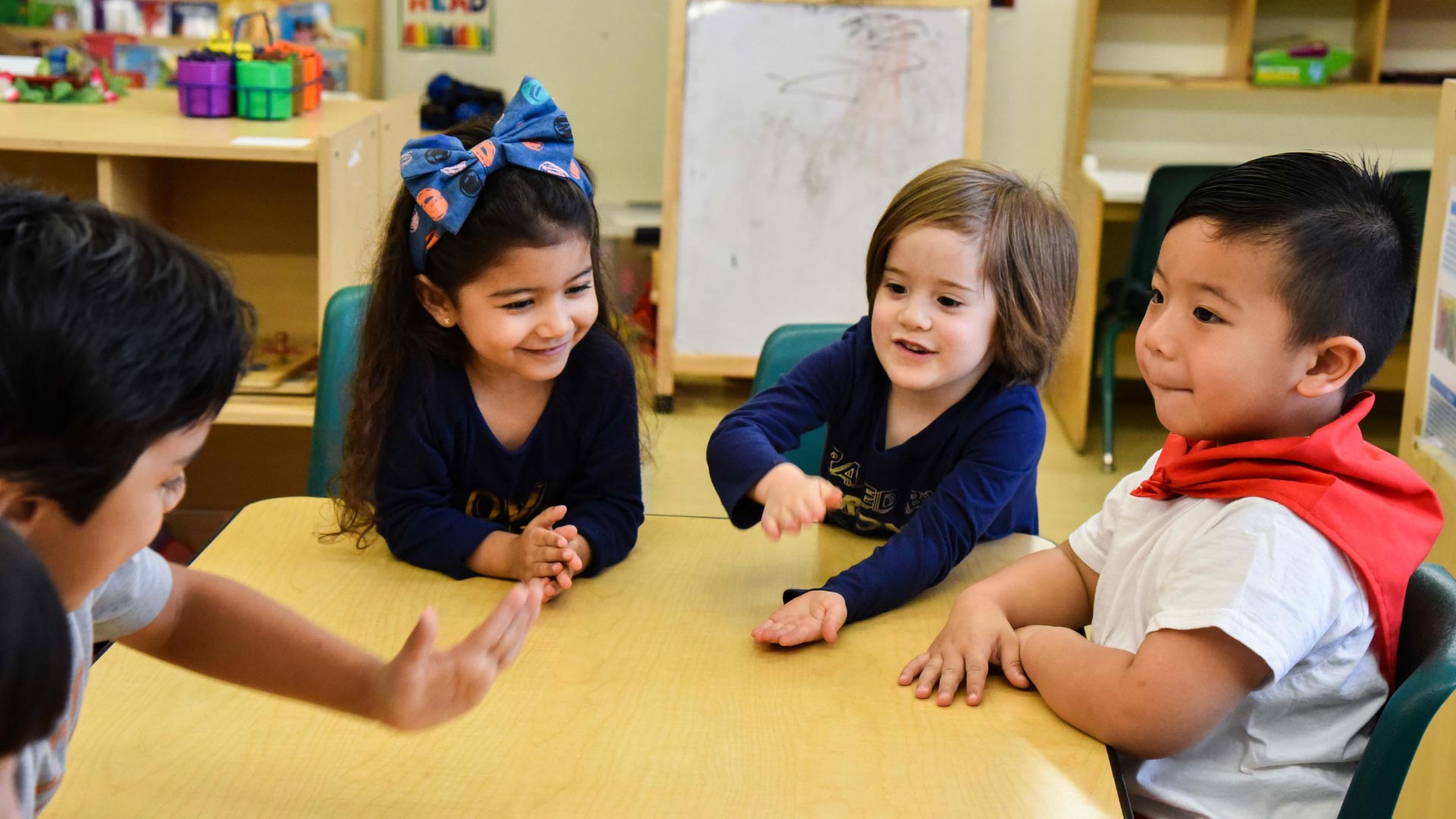 Four children at a head start preschool seated around the table playing and talking.