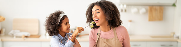 Child feeding parent salad with both smiling