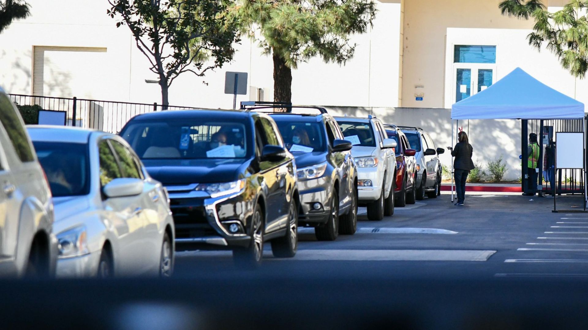 A line of cars at the Chatsworth office location with a staff member checking them in in the distance.