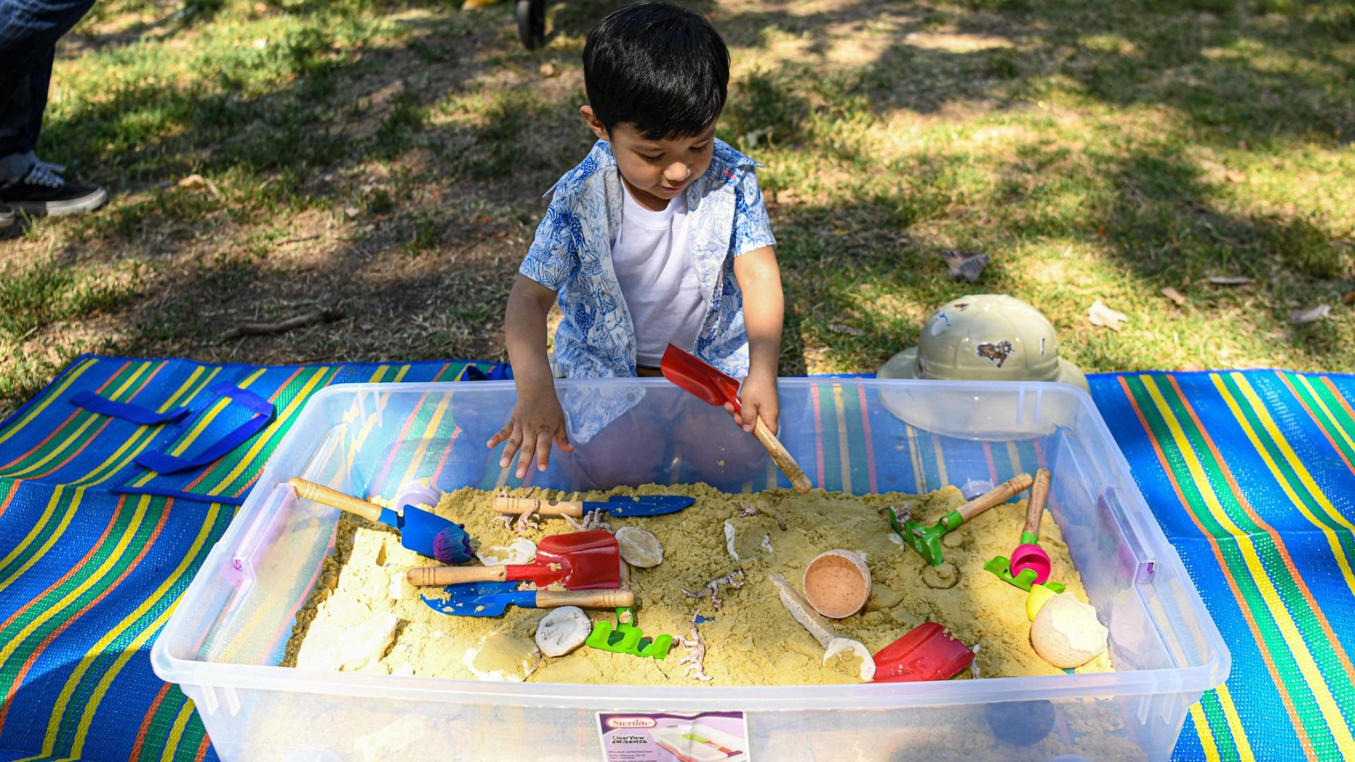 A 5 year old boy playing in a sandbox outside in the park.