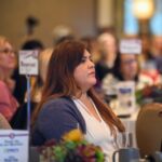 Female sitting and at a reserved table listening to a speak who is off camera.