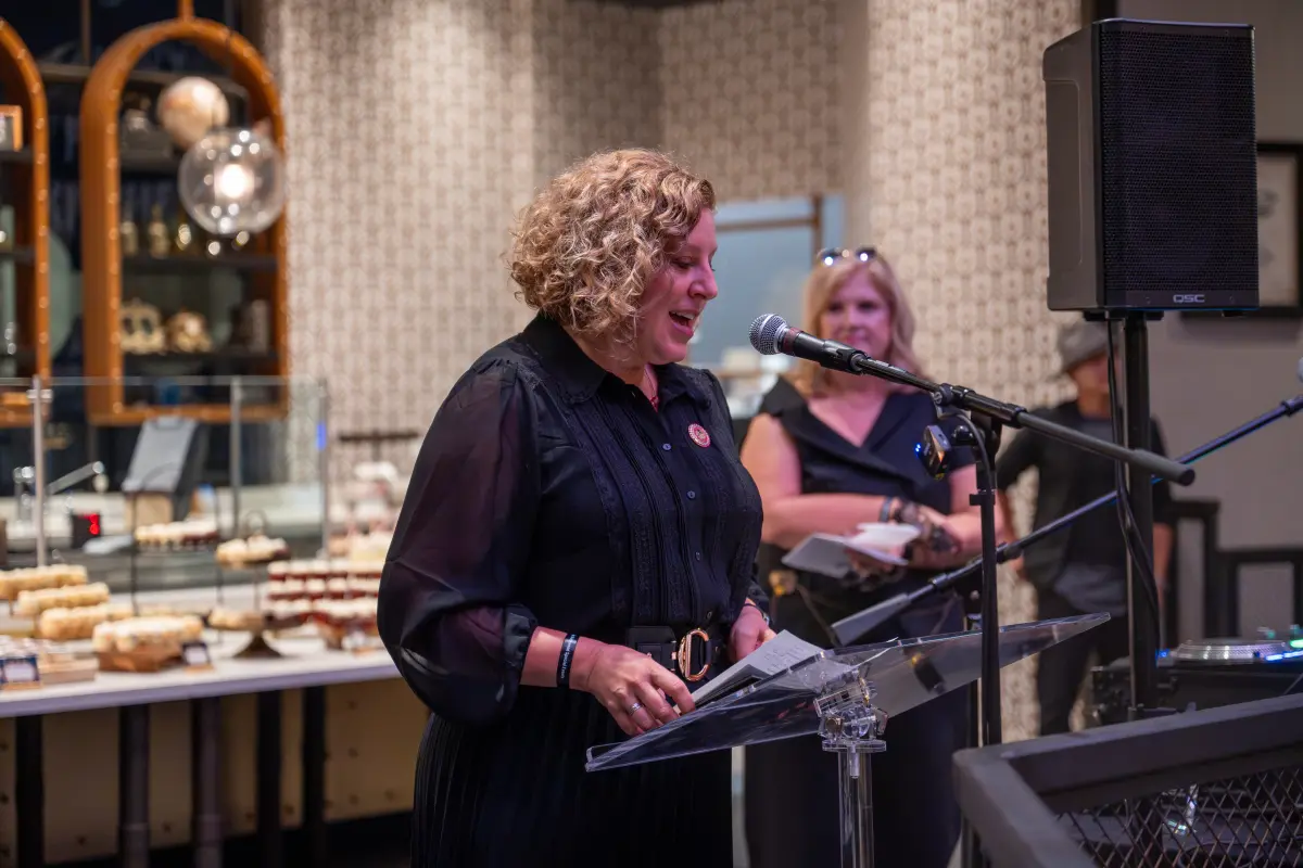 Assemblymember Pilar Schiavo speaking into a microphone to guests at The Toothsome Chocolate Emporium & Savory Feast Kitchen