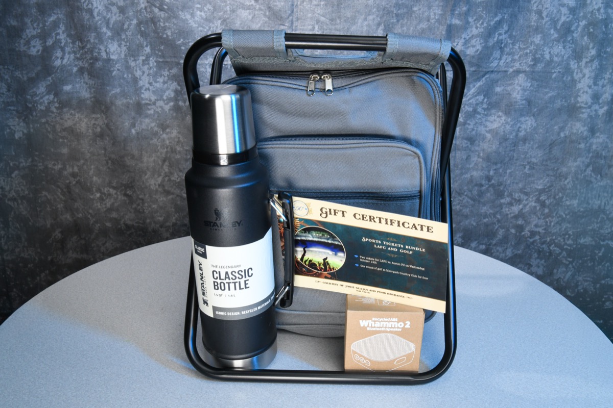 A black Stanley Classic Bottle is prominently displayed on a metal stand next to a gray cooler bag, a gift certificate for sports tickets, and a box of a Whammo 2 Bluetooth speaker.
